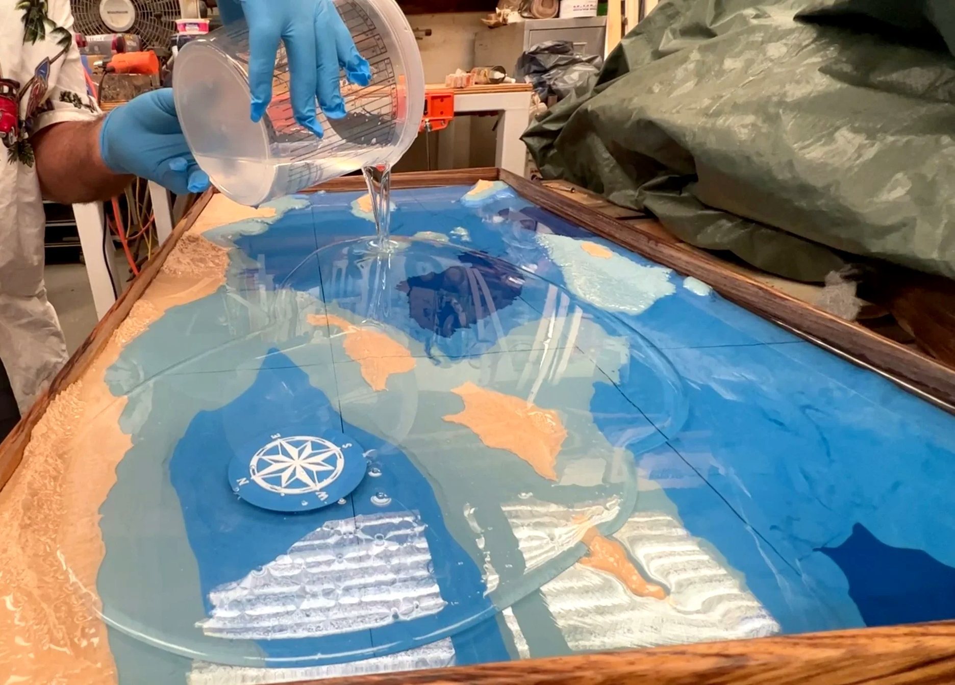 Clear resin being poured over a bathymetric relief set into a timber table frame